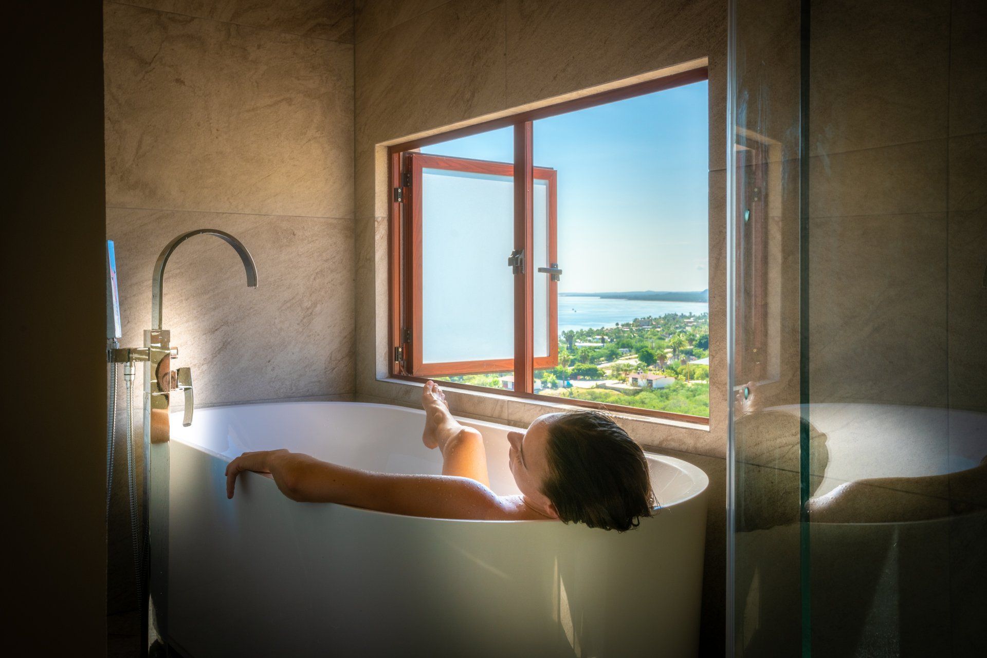 A woman is taking a bath in a bathtub with a view of the ocean.