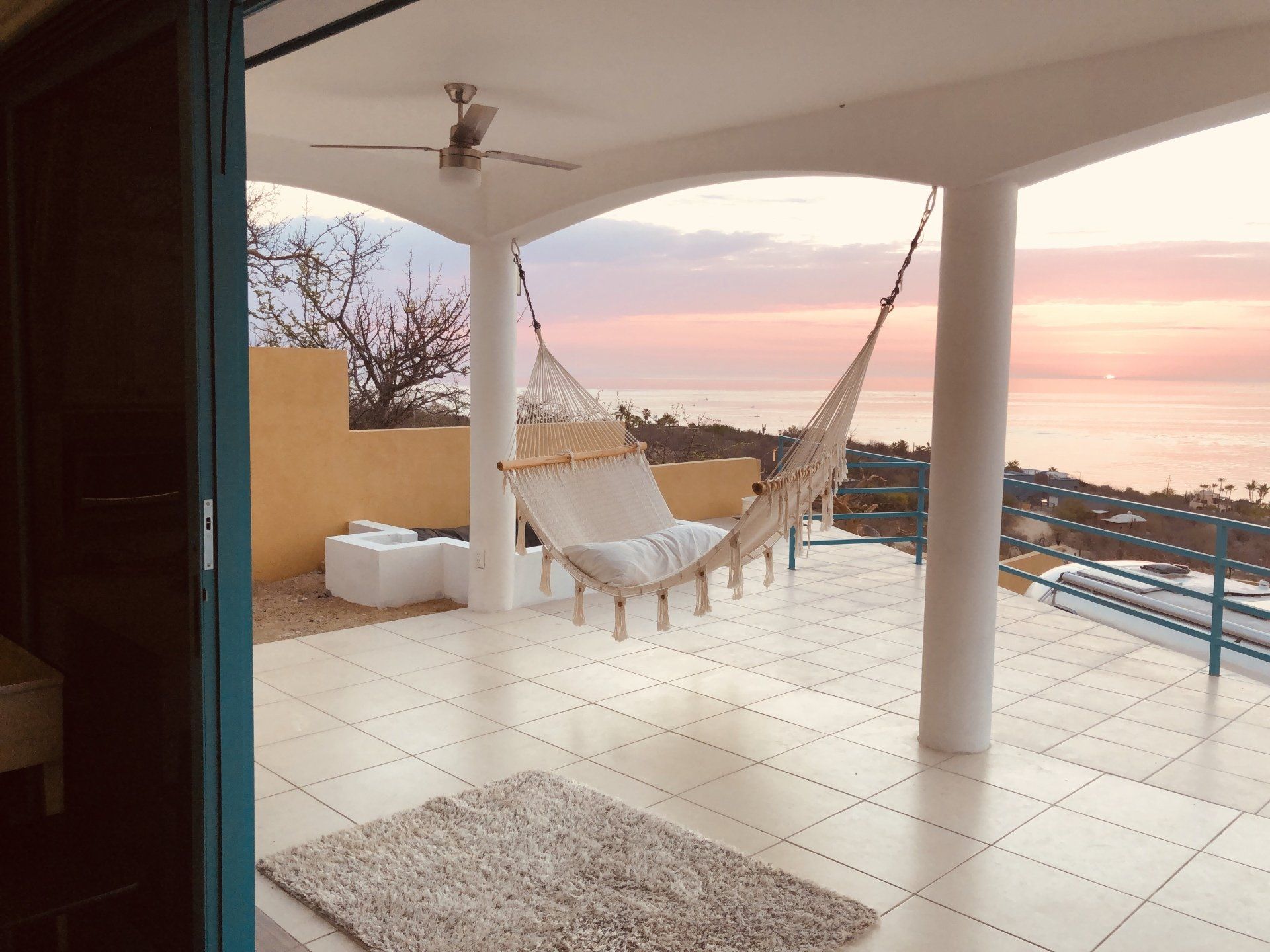 A hammock is hanging on a balcony overlooking the ocean.