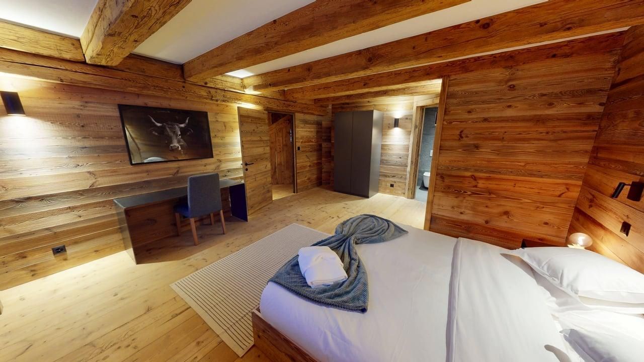 Une chambre rustique en bois avec un lit blanc, un bureau et une chaise, et un tableau de taureau au mur.
