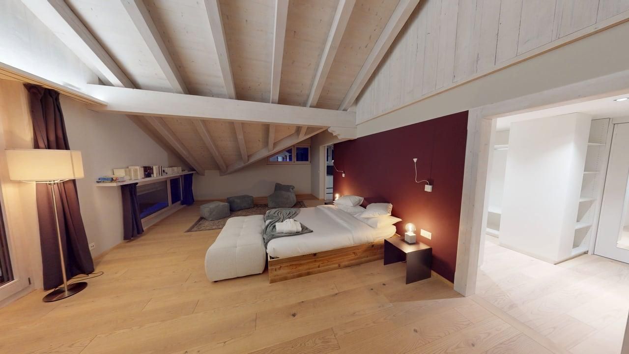 Une chambre mansardée spacieuse et moderne, avec un lit aux draps blancs, un mur d'accent bordeaux et un parquet clair.