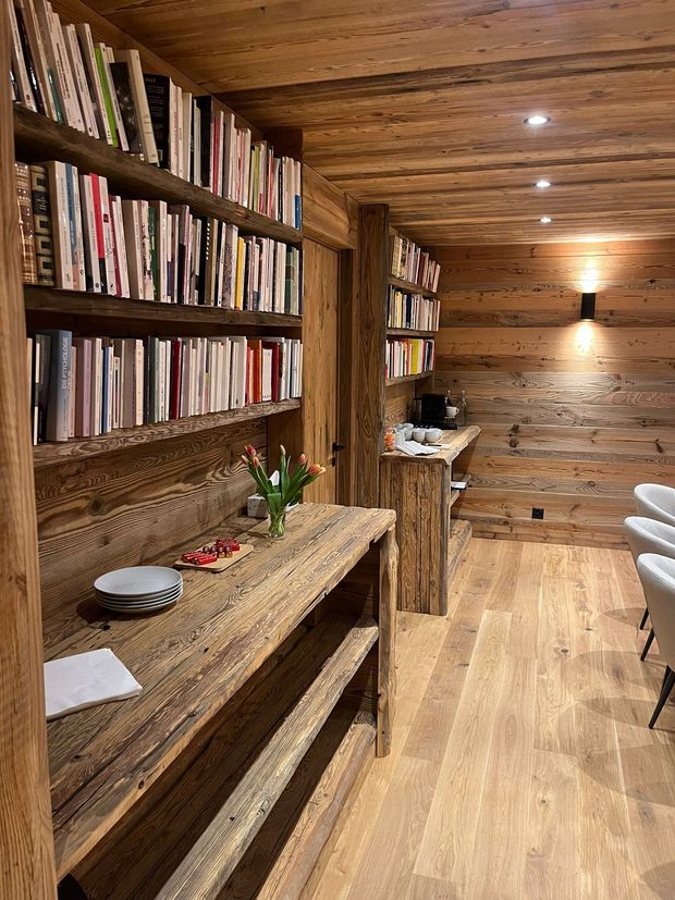 Une bibliothèque chaleureuse avec des murs lambrissés rustiques, des étagères allant du sol au plafond et une longue console en bois.