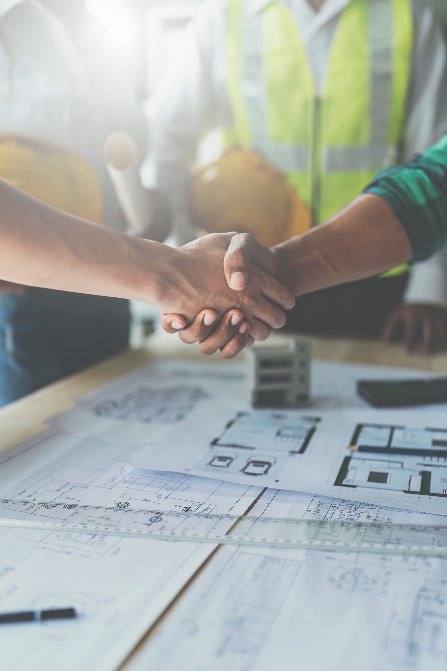 Gente dándose la mano sobre planos en obra.