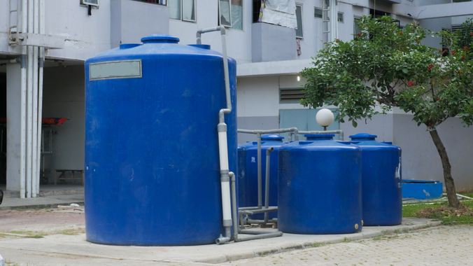 A row of blue water tanks are sitting in front of a building.