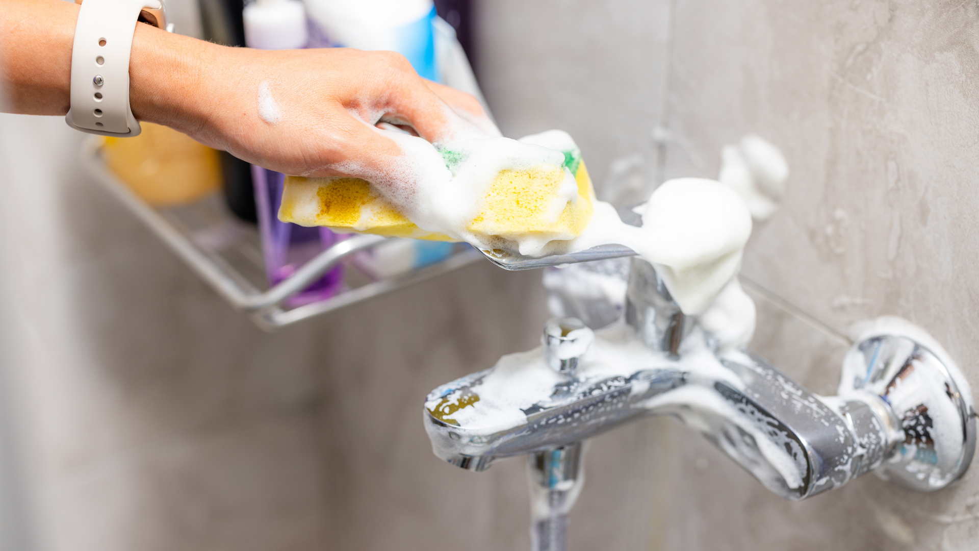 A person is cleaning a bathroom faucet with a sponge.