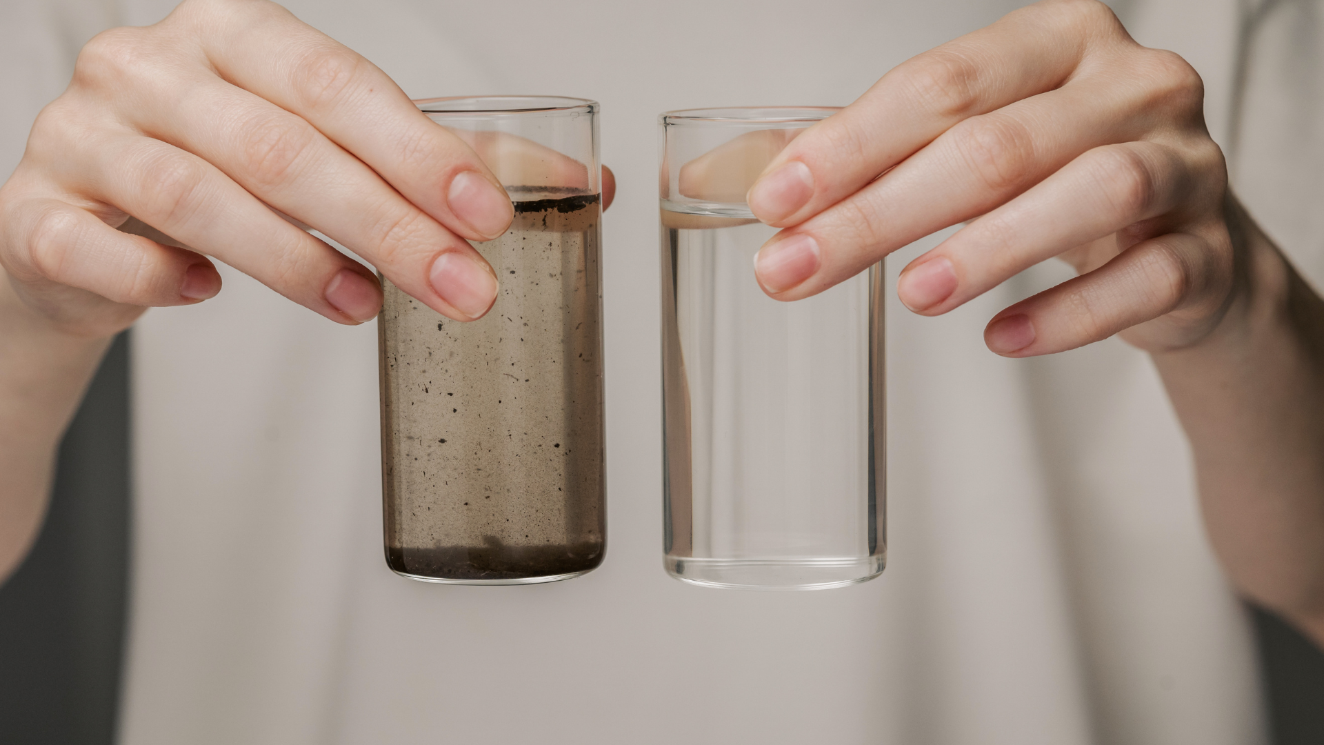 A person is holding two glasses of water in their hands.
