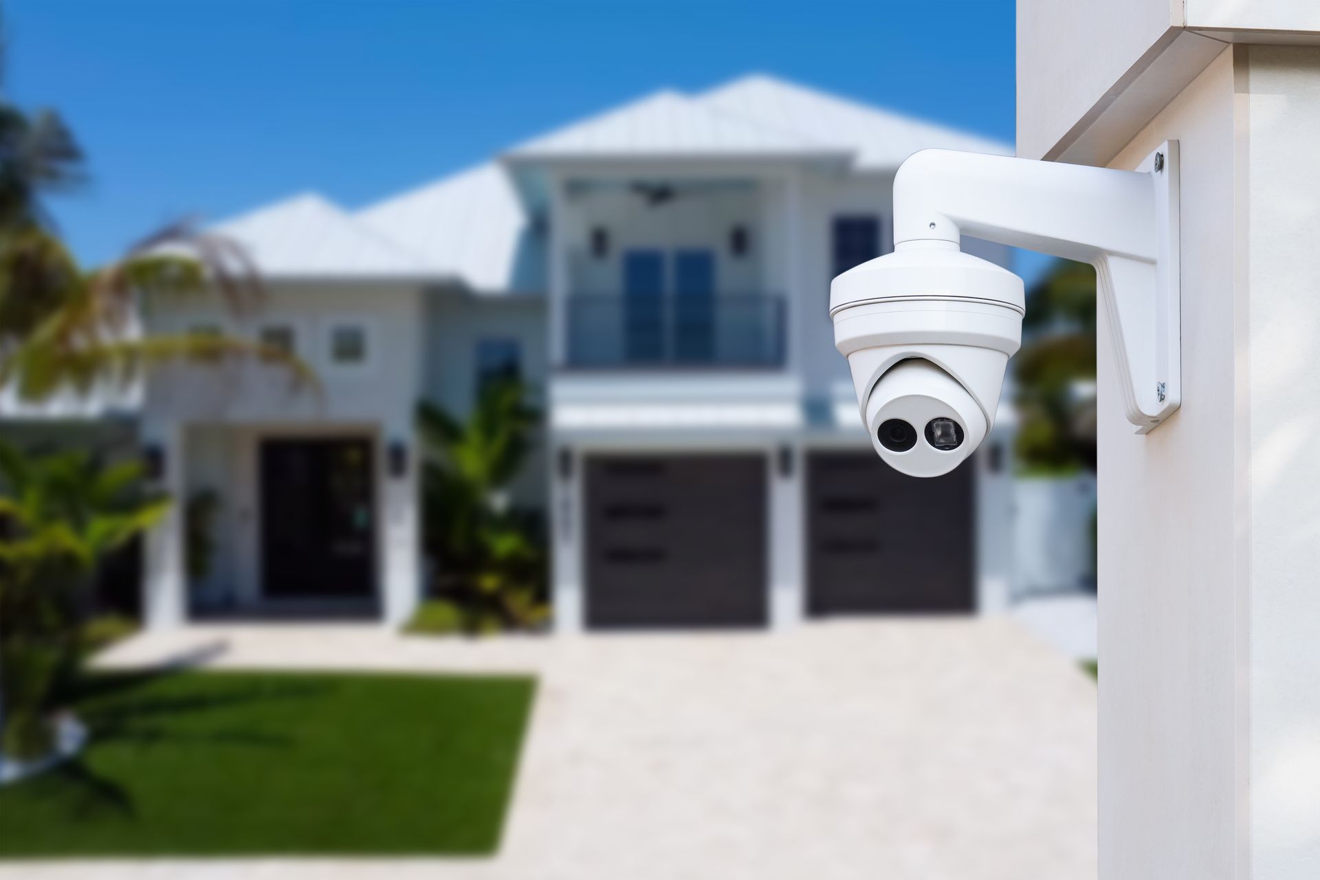 A security camera is mounted on the side of a building in front of a house.