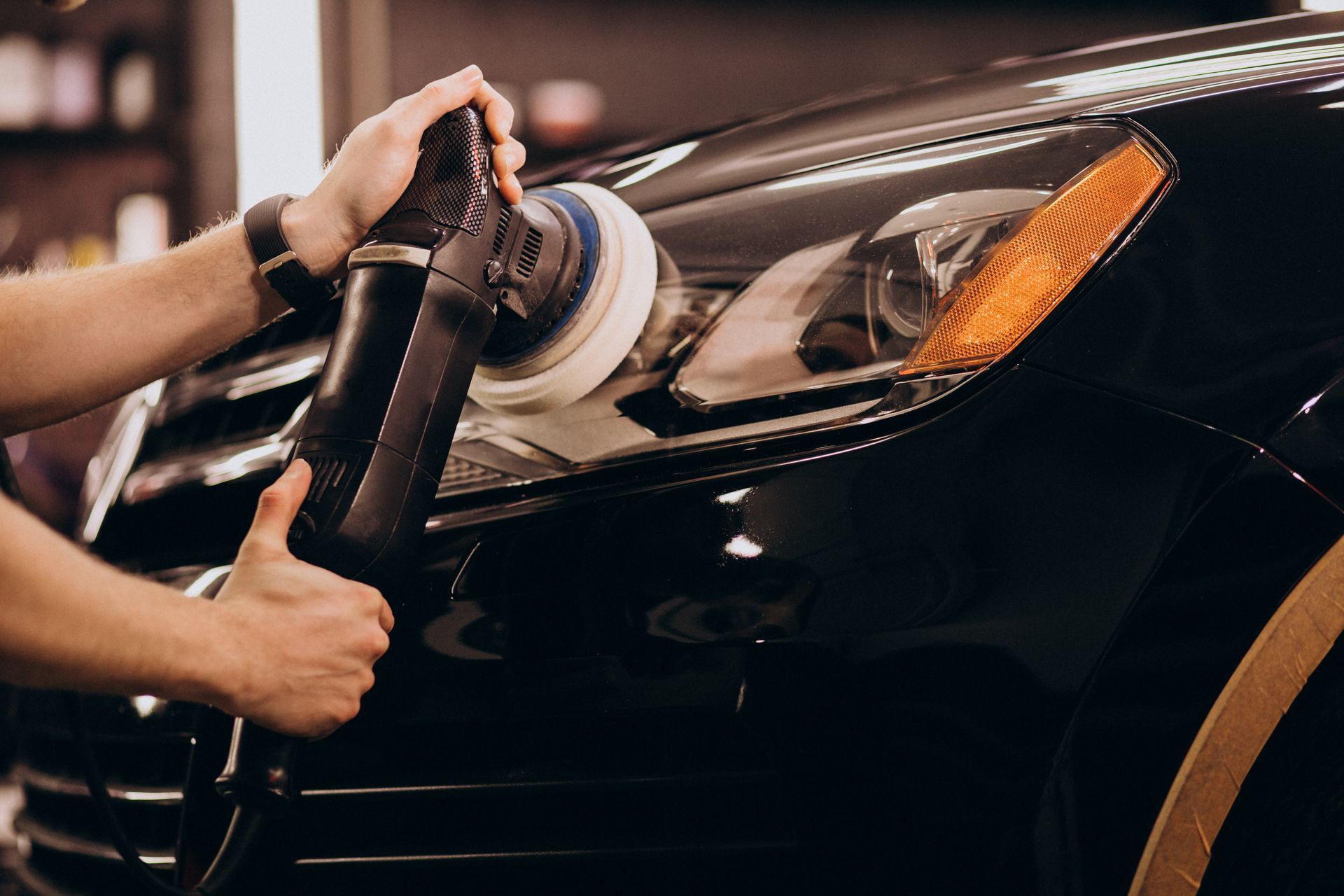 A man is polishing the headlight of a black car.