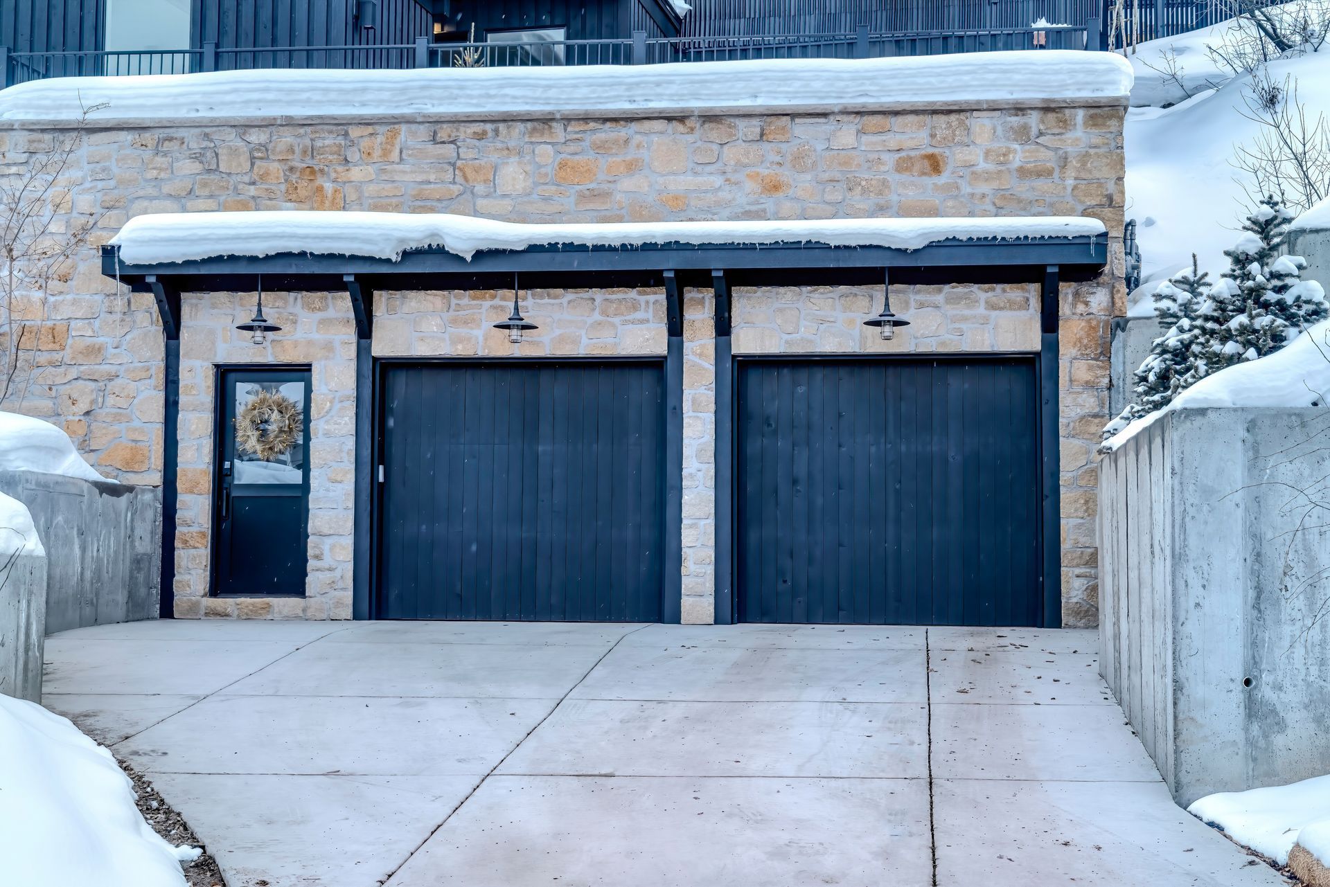 Stone garage with dark blue doors and a small window, covered in snow.