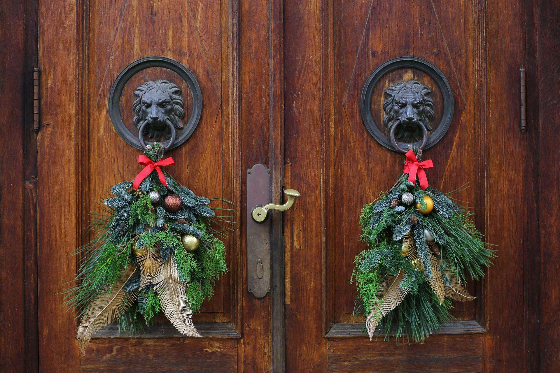 Ornate wooden doors with lion-head door knockers, decorated with greenery and ornaments for the holidays.