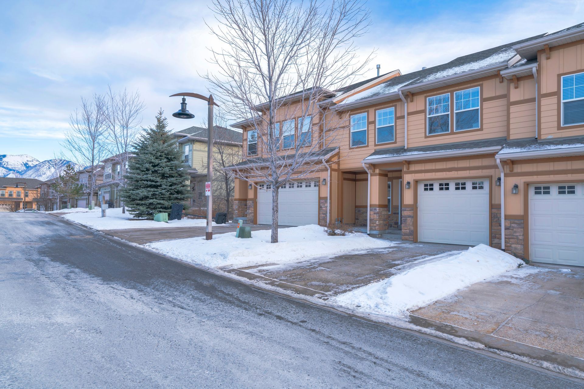Row of townhouses with snow-covered driveways and road on a cloudy winter day.
