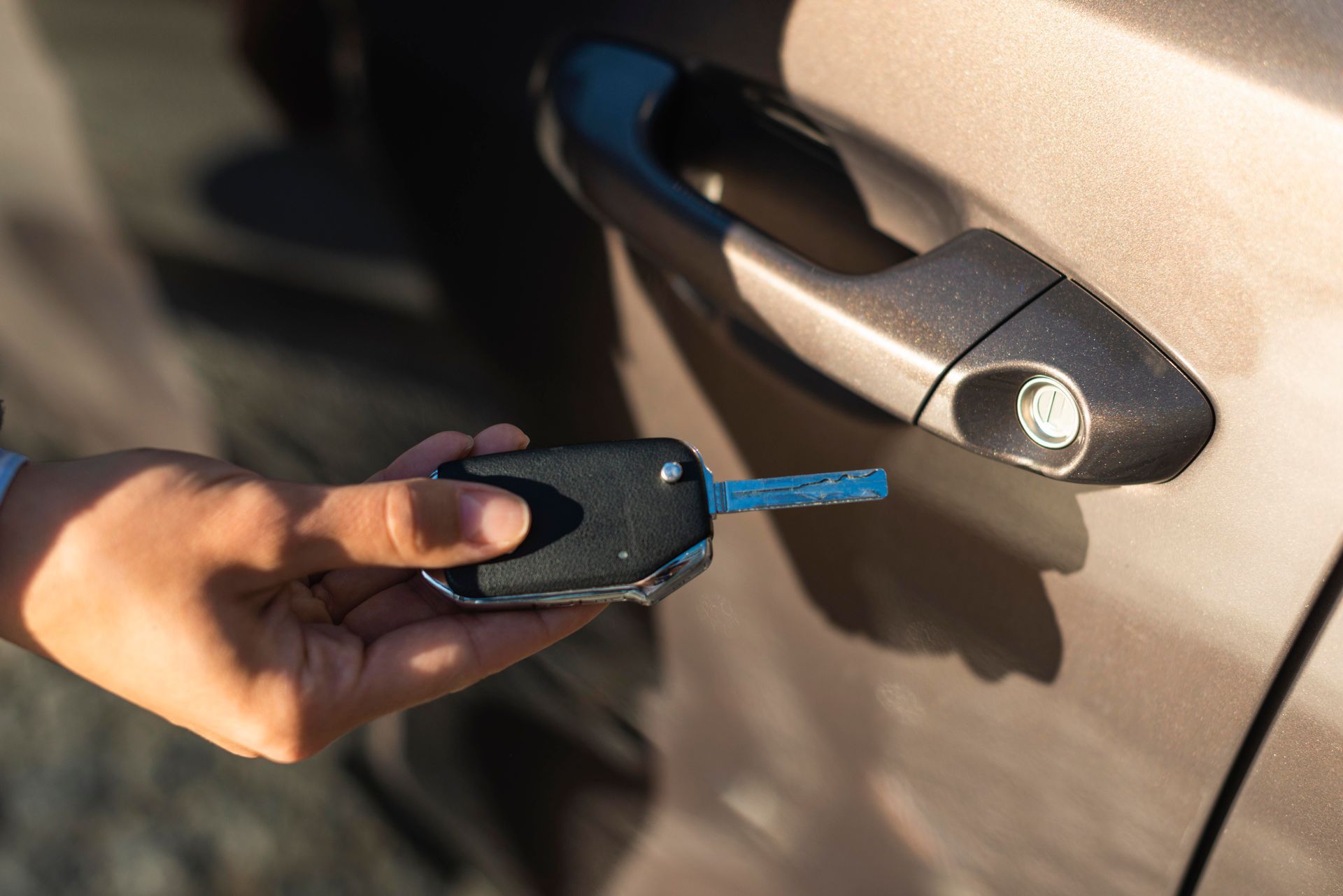 A person is holding a car key in front of a car door.