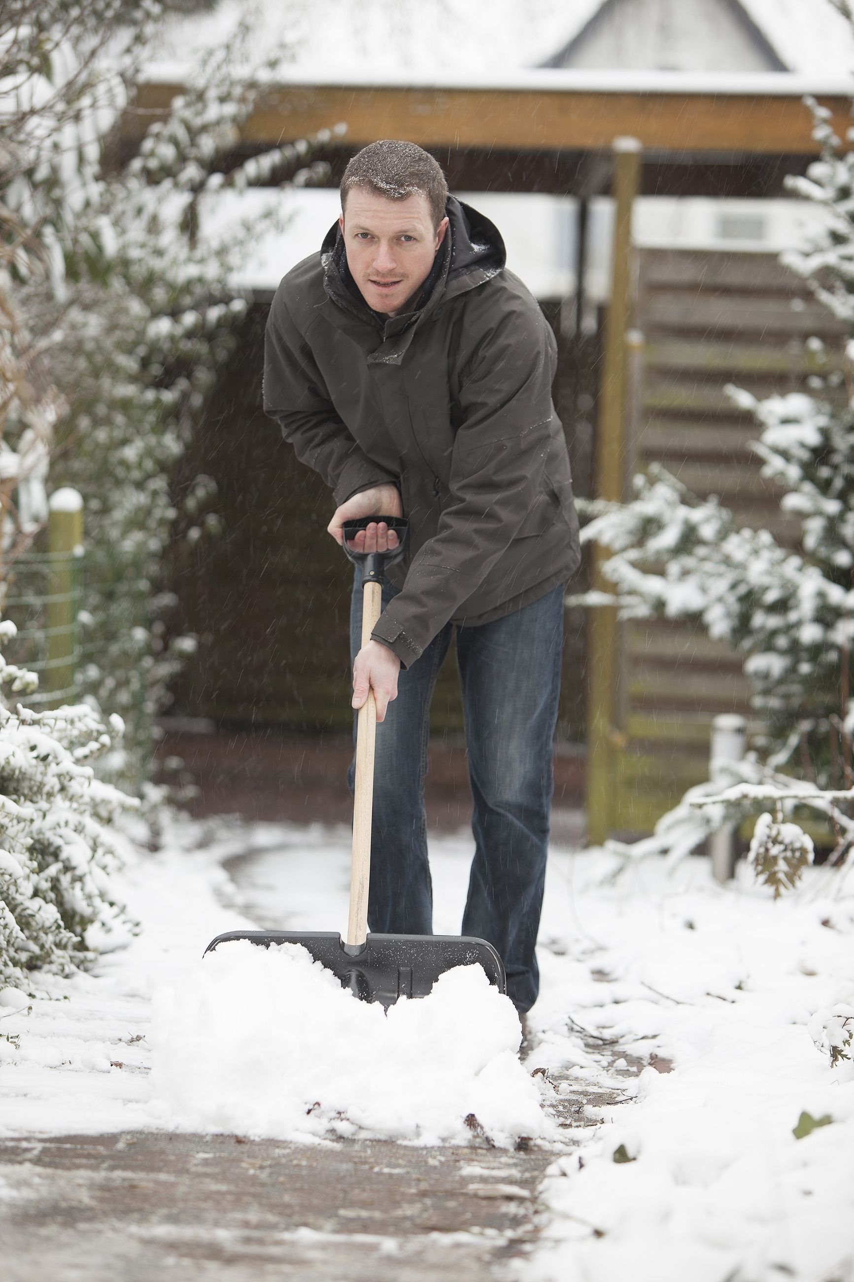 A man is shoveling snow from a sidewalk with a shovel.