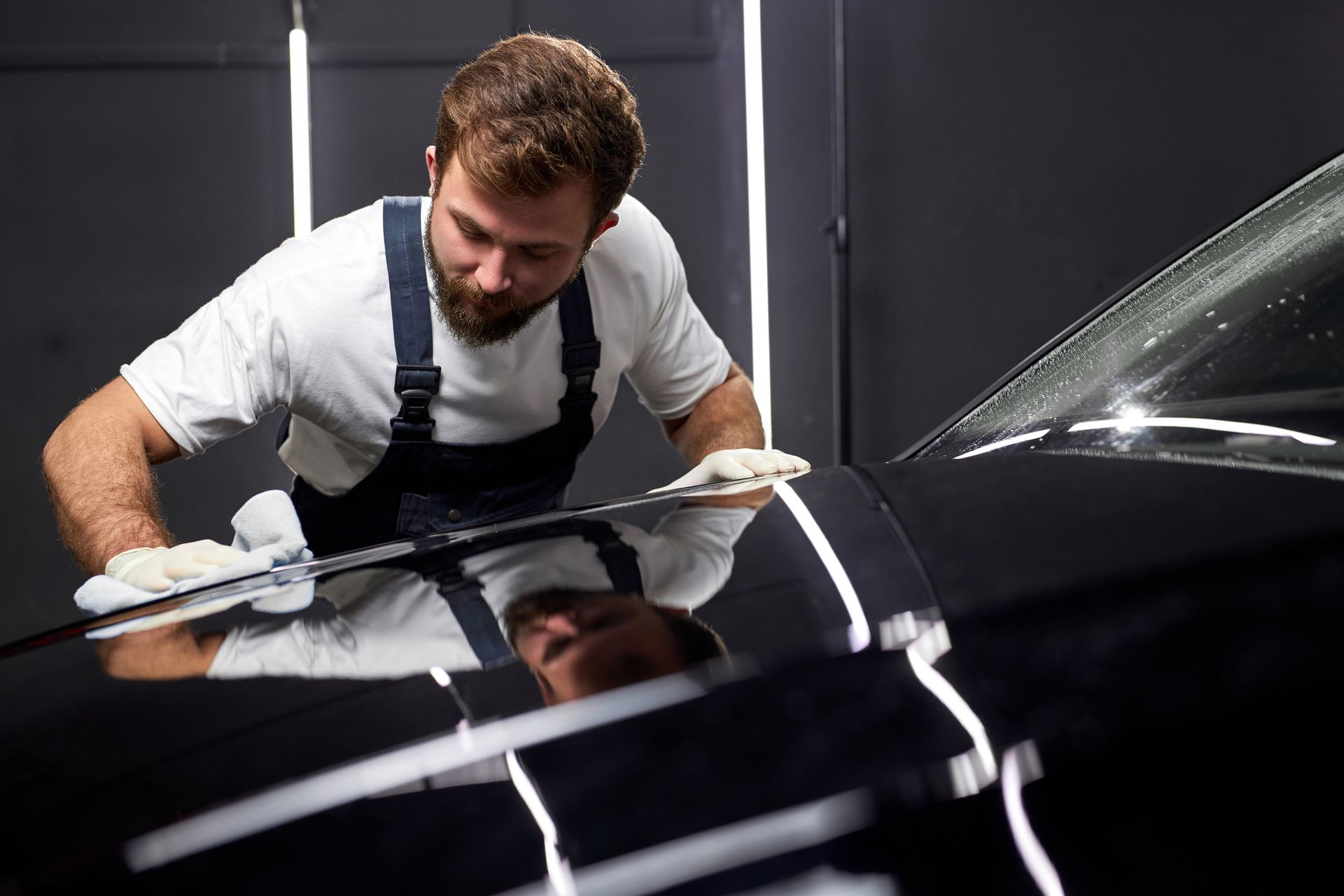 A man is polishing the hood of a black car.