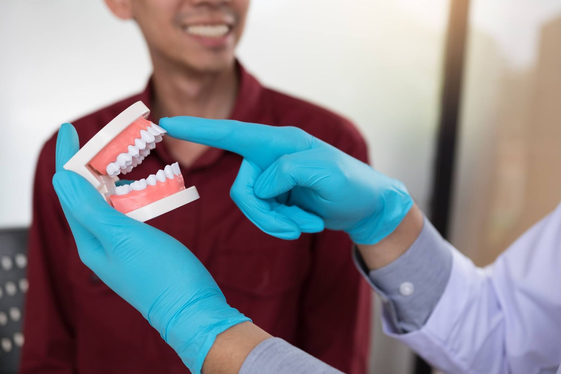 Dentist Demonstrating Dental Model to Smiling Patient, Hands in Blue Gloves.