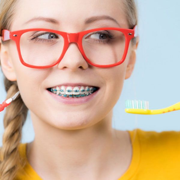 Woman With Braces And Glasses Is Brushing Her Teeth — Dentist On Tweed in Tweed Heads, NSW