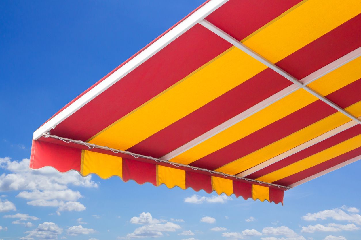 Toldo de rayas rojas y amarillas contra un cielo azul con nubes.