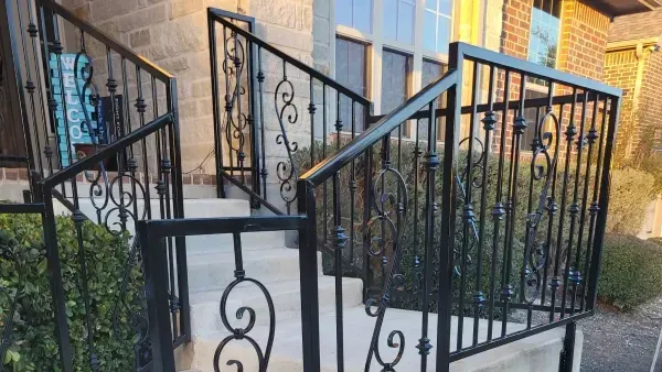 A wrought iron railing surrounds a set of stairs leading up to a house.