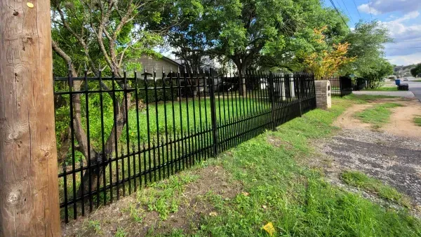 A black wrought iron fence surrounds a lush green field.