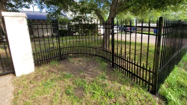 A black wrought iron fence is surrounded by grass and trees.