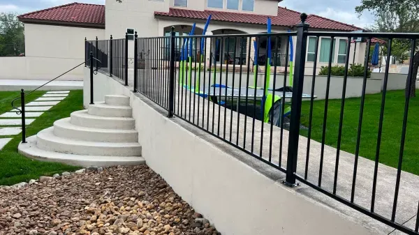 A black metal fence surrounds a staircase leading to a house.