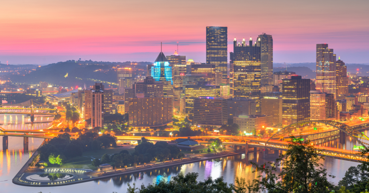 Pittsburgh city skyline at sunset with illuminated bridges, reflecting on the river.