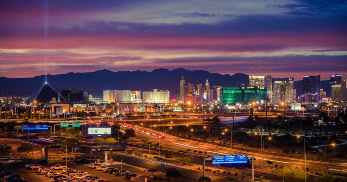 Scenic view of the Las Vegas Strip at sunset with city lights, hotels, and mountains in the background.