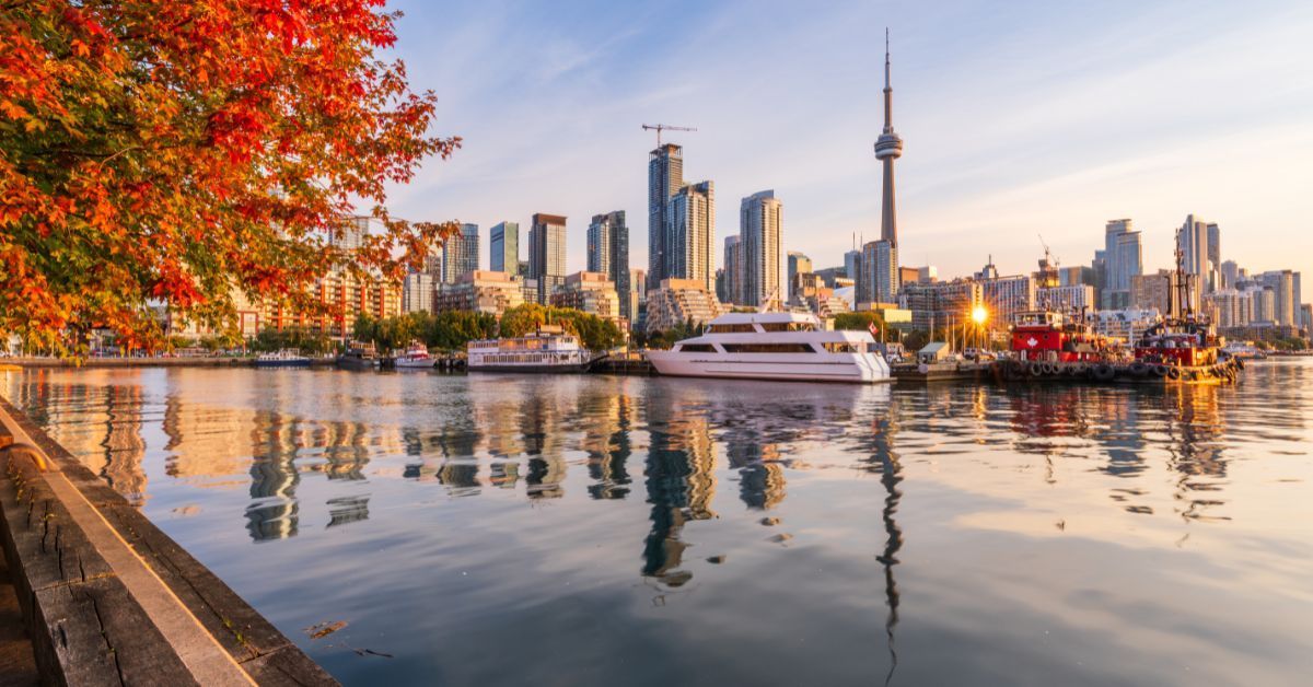 Toronto skyline at sunset during autumn, featuring colorful fall leaves, waterfront reflections, and the CN Tower in Ontario, Canada.