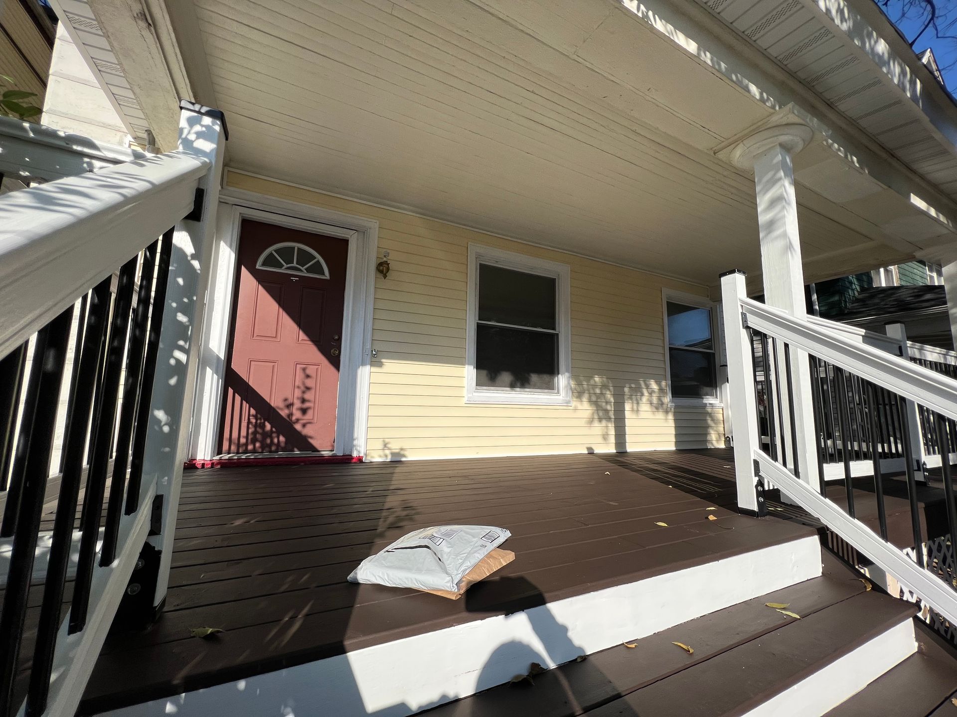 The front porch of a house with a red door and white railing