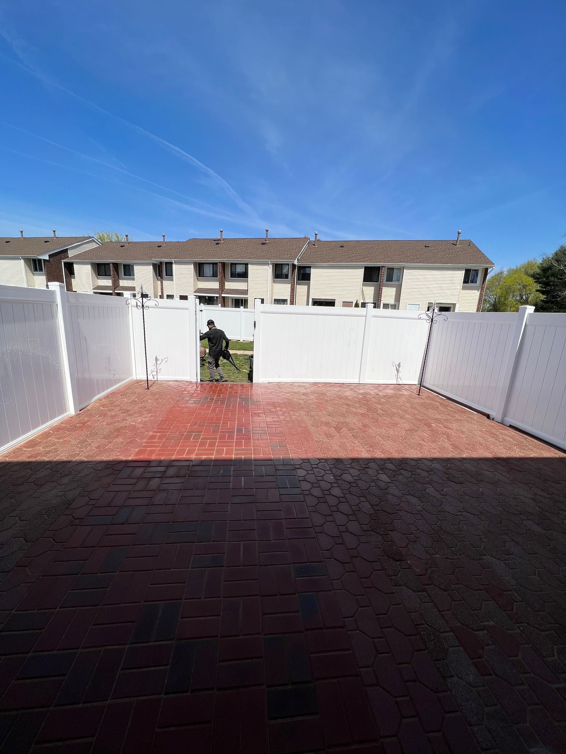 A white fence surrounds a brick driveway in front of a row of houses.