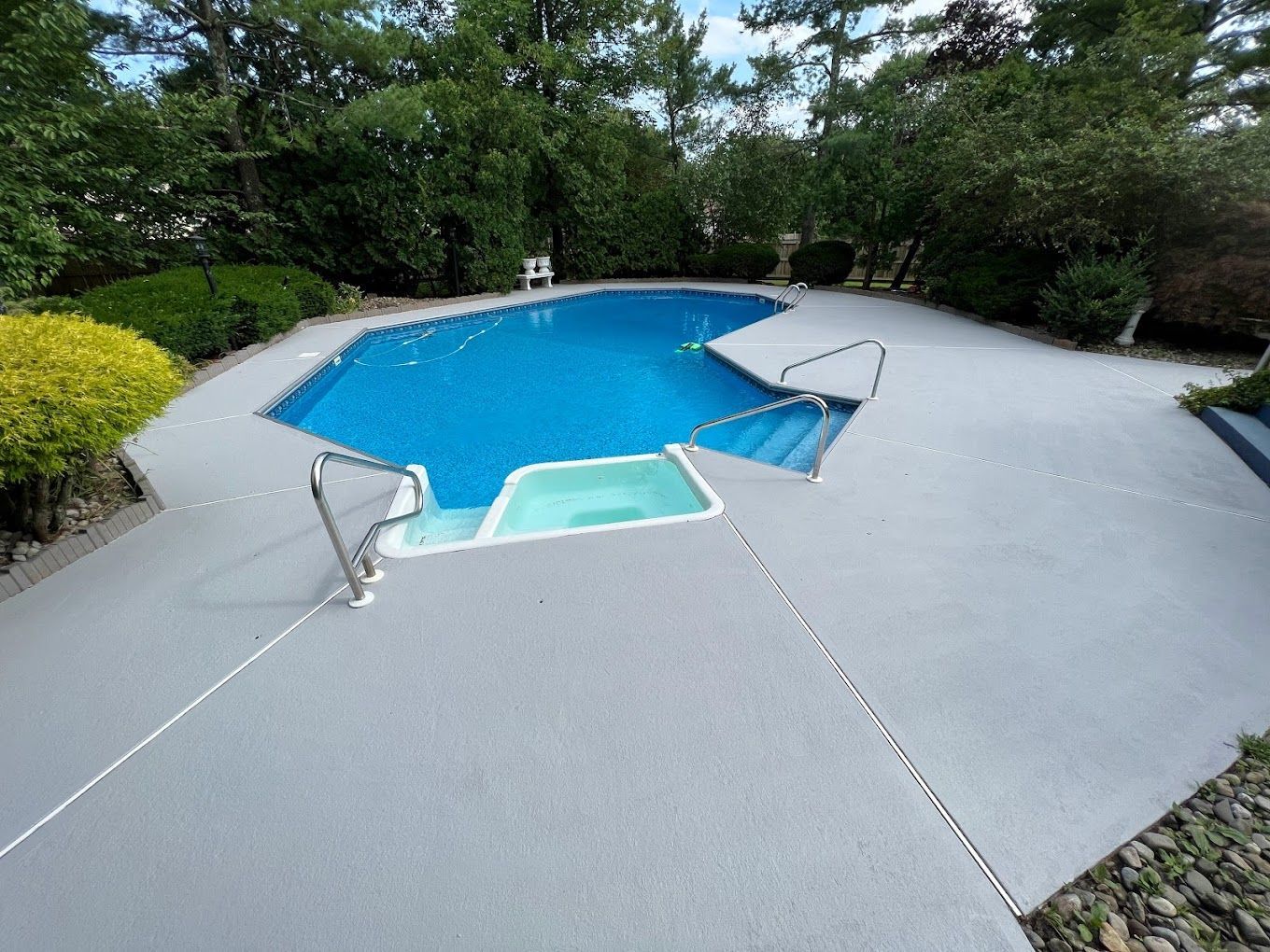 A large swimming pool surrounded by trees and a concrete deck.