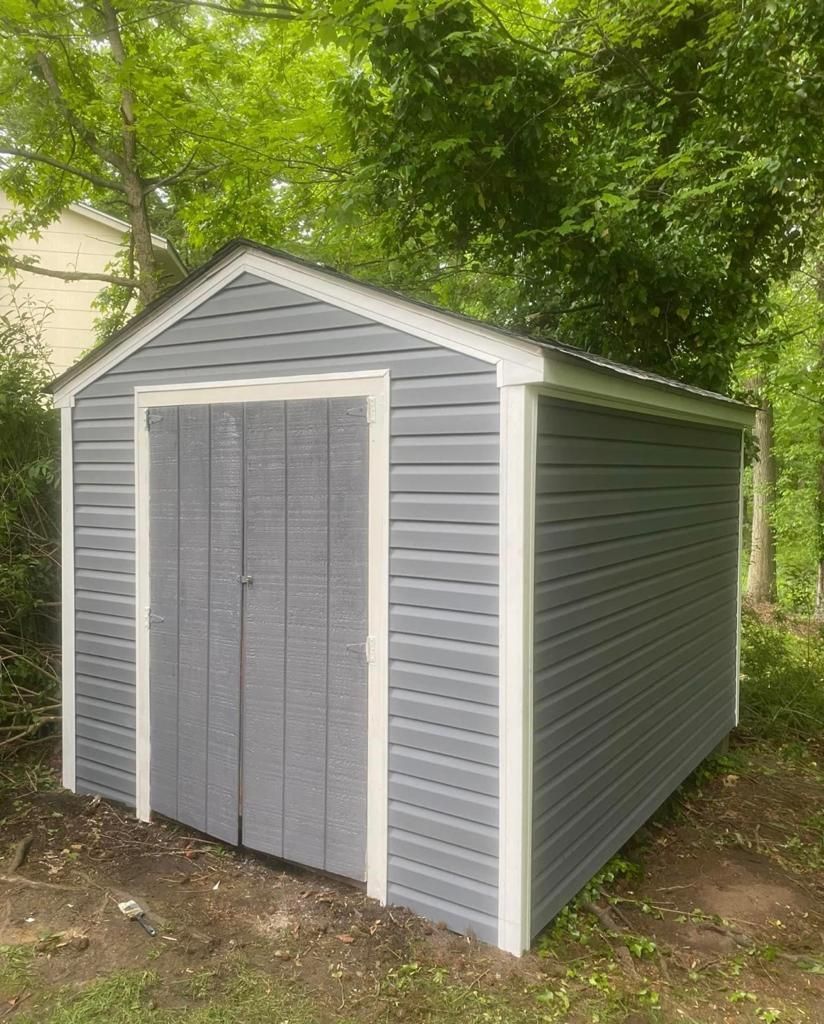 A gray and white shed is sitting in the middle of a yard.