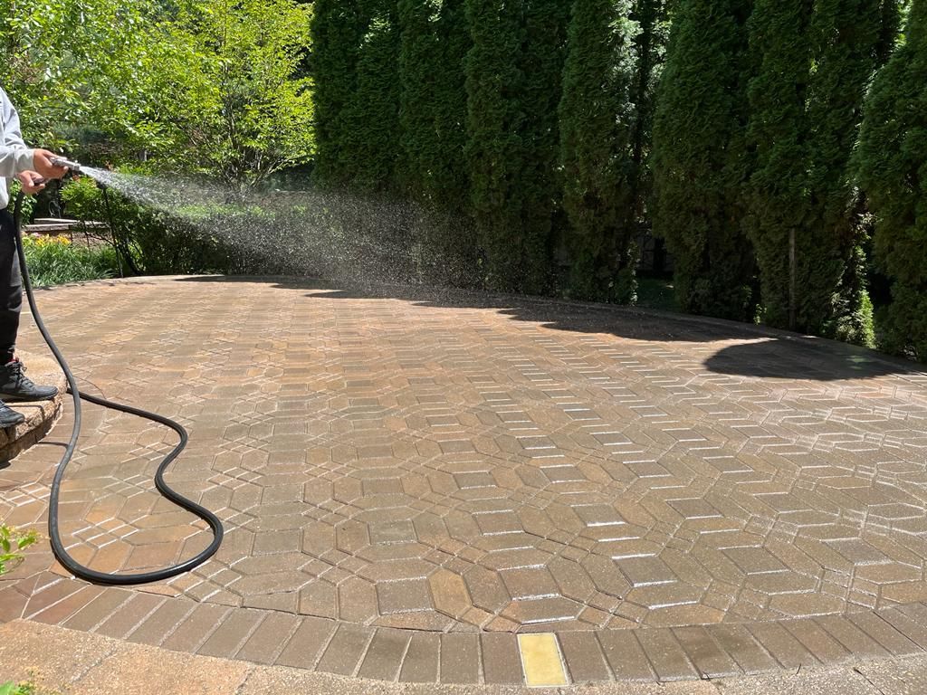 A man is spraying water on a brick driveway with a hose.