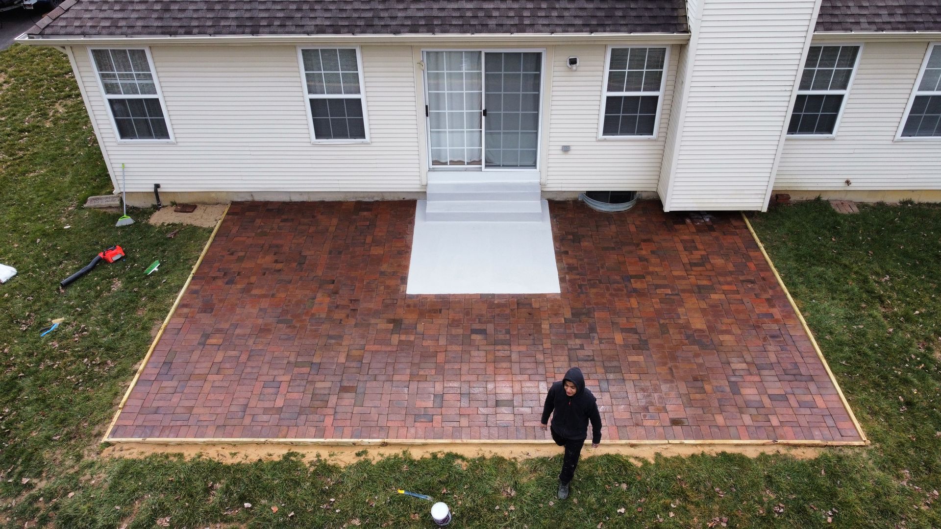 An aerial view of a person walking on a brick patio in front of a house.