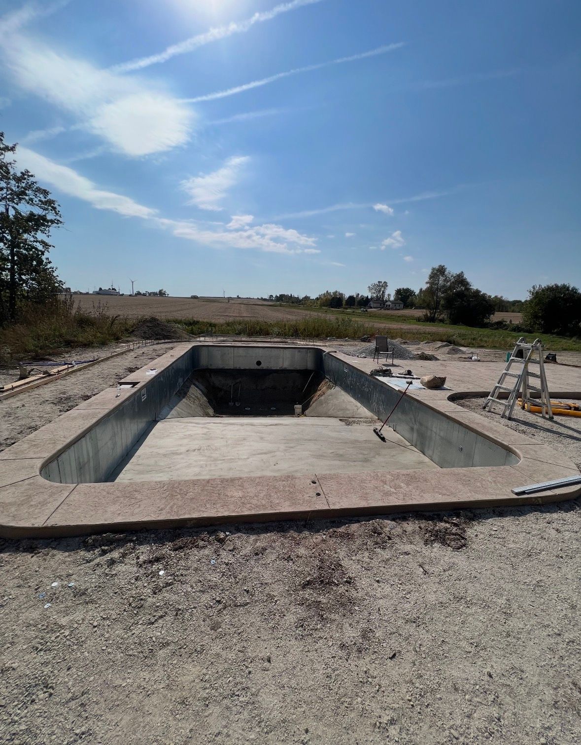 An empty, rectangular in-ground swimming pool under construction, surrounded by gravel on a sunny day.