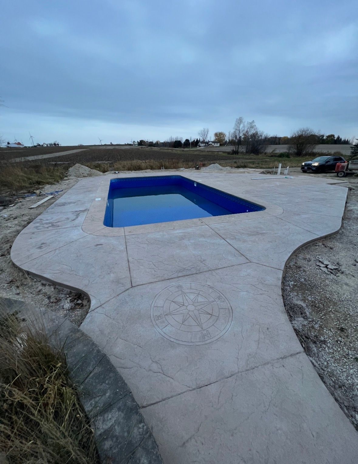 An outdoor, in-ground blue rectangular swimming pool surrounded by a freshly poured, light-gray concrete patio.