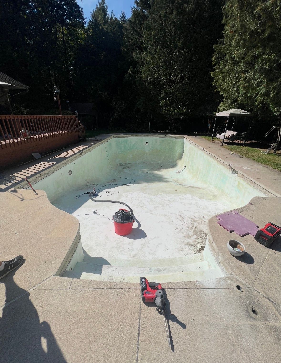 An empty, light-green swimming pool under construction with a red shop vacuum and a power tool on the patio deck.