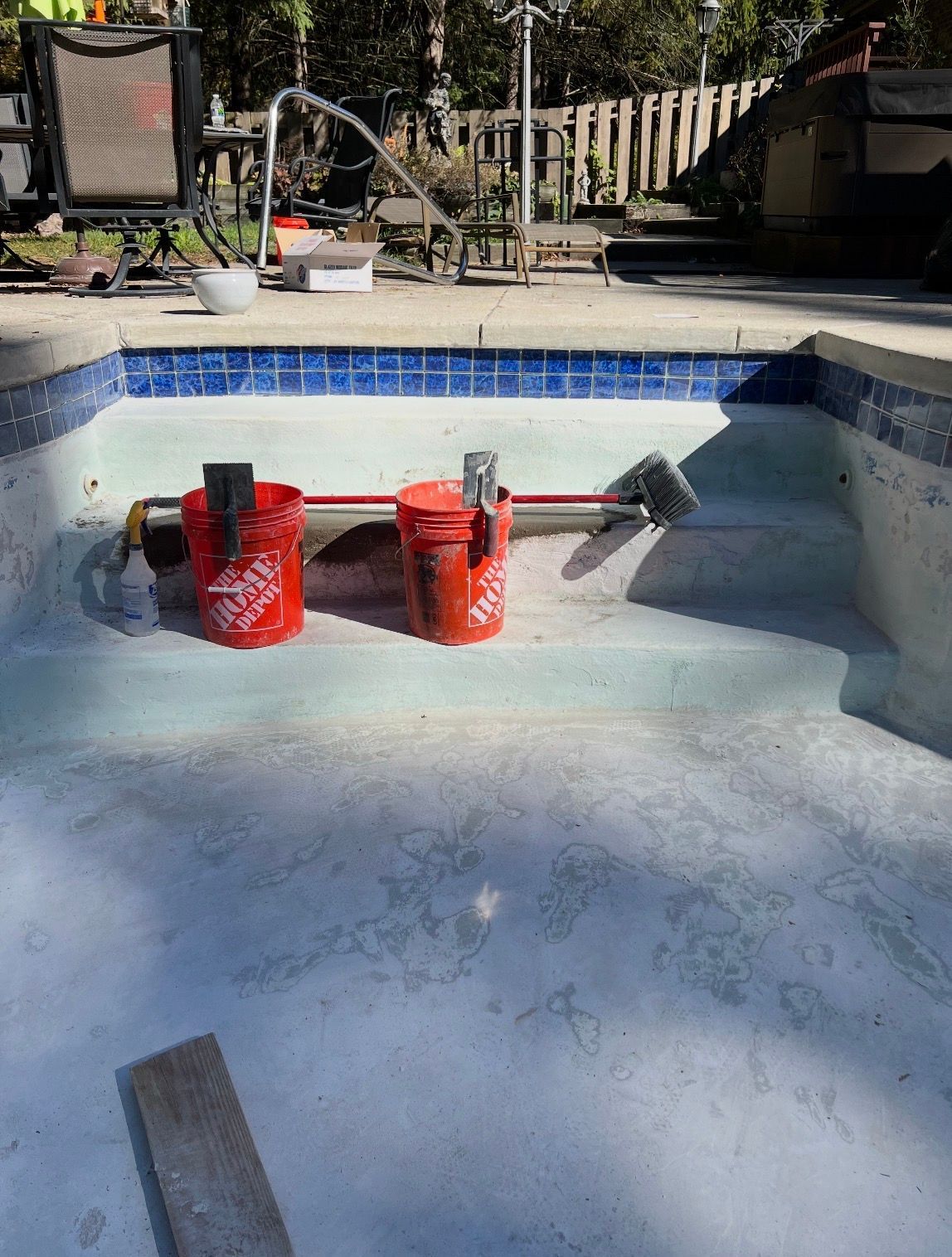 Two orange buckets and pool cleaning equipment sit on the steps of an empty, tiled swimming pool.
