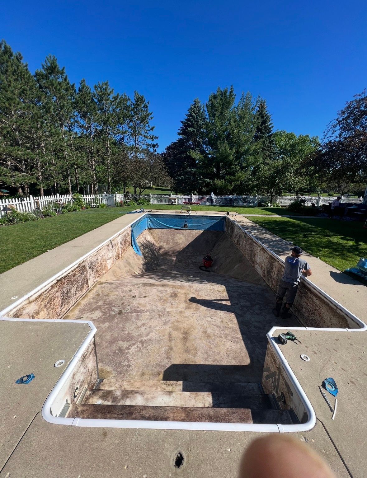 An empty rectangular backyard swimming pool undergoing renovation with a worker standing on the edge.