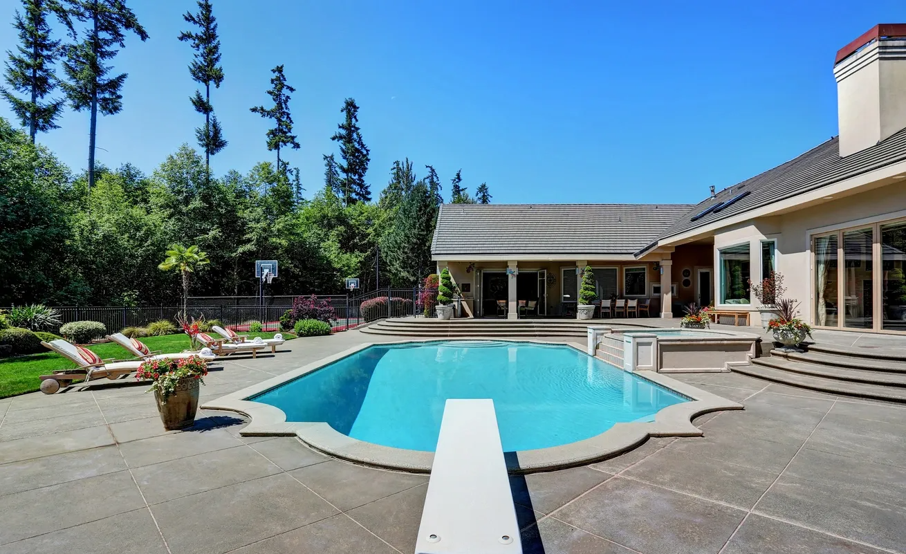 A large swimming pool is in the backyard of a house.