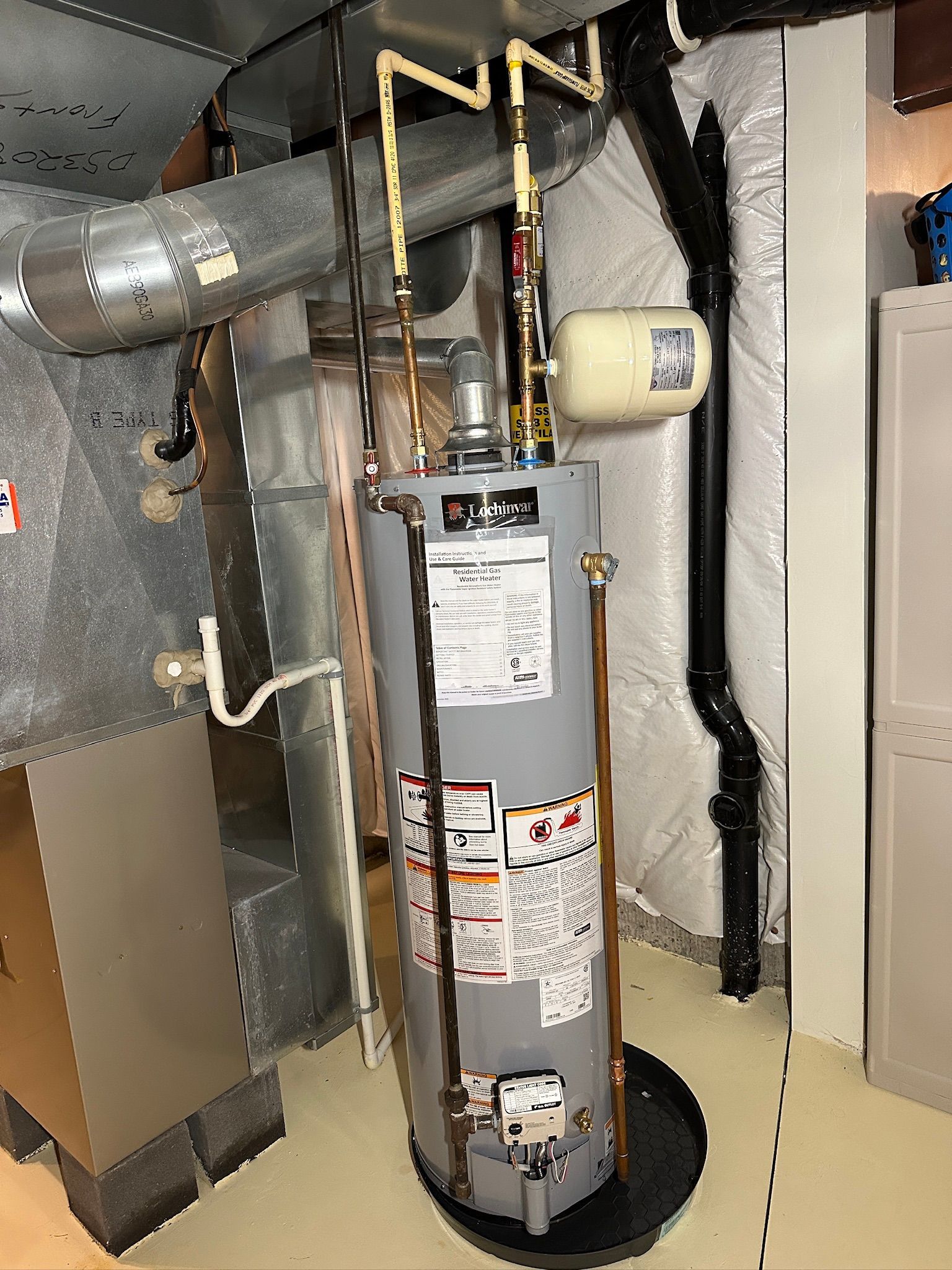 Plumber repairing a water heater under a sink, using a wrench and inspecting exposed pipes.