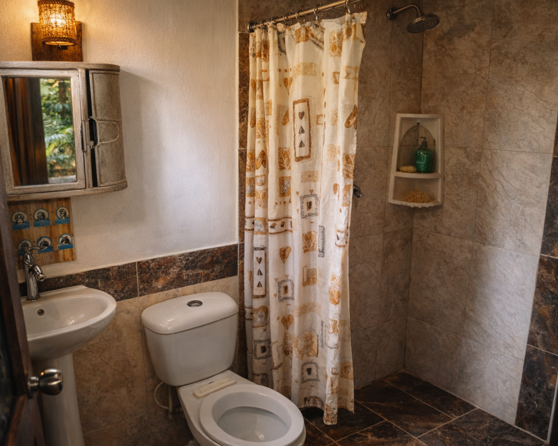 Baño con inodoro, lavabo y ducha. Azulejos color canela, cortina de ducha estampada y mueble de pared.