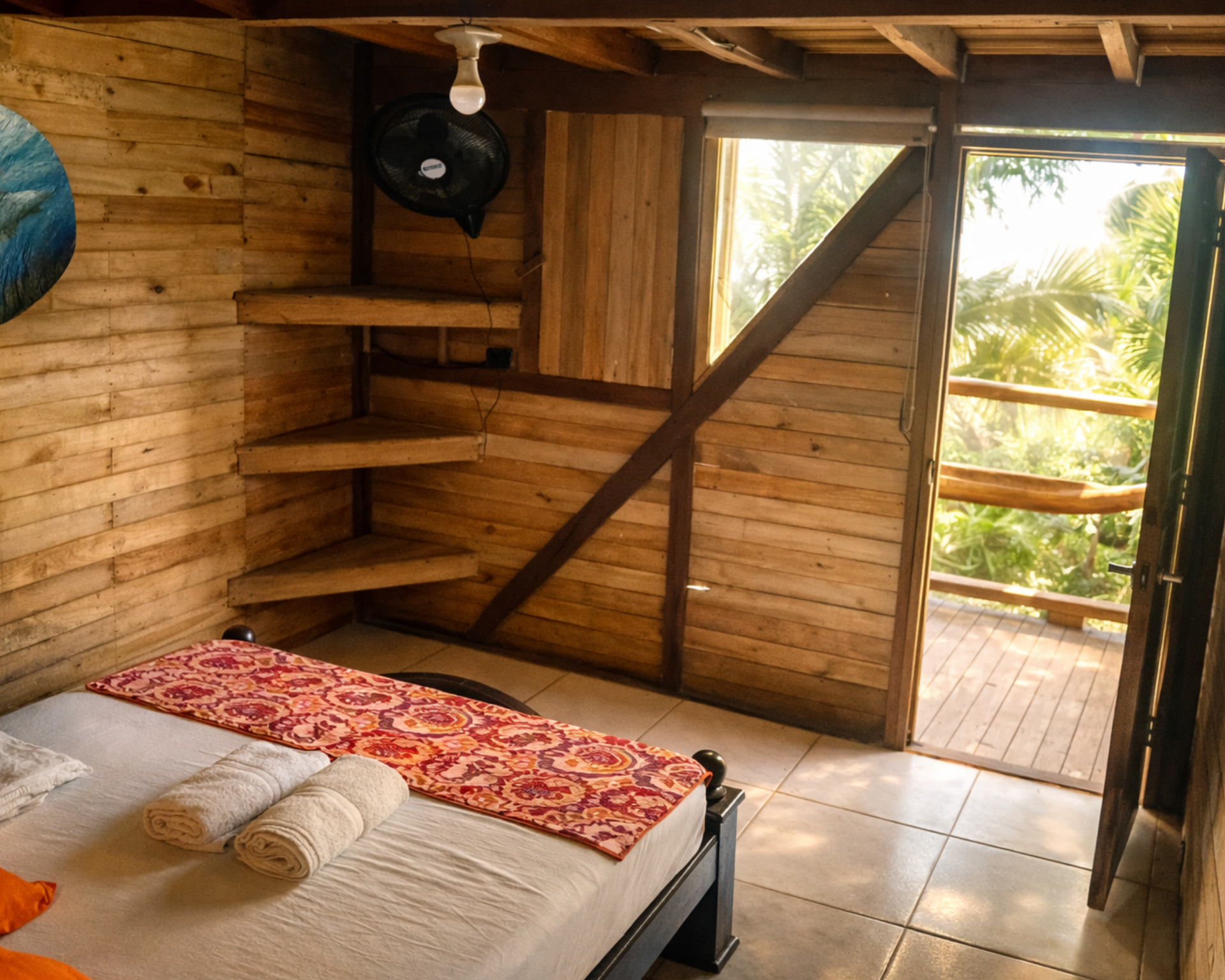 Interior de cabaña de madera con cama, toallas y balcón con vista a la vegetación.