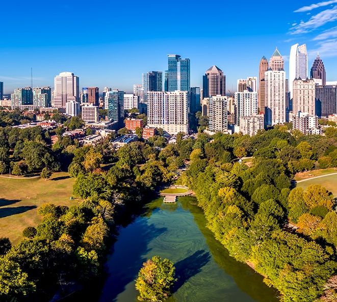 An aerial view of a river running through a park with a city skyline in the background.