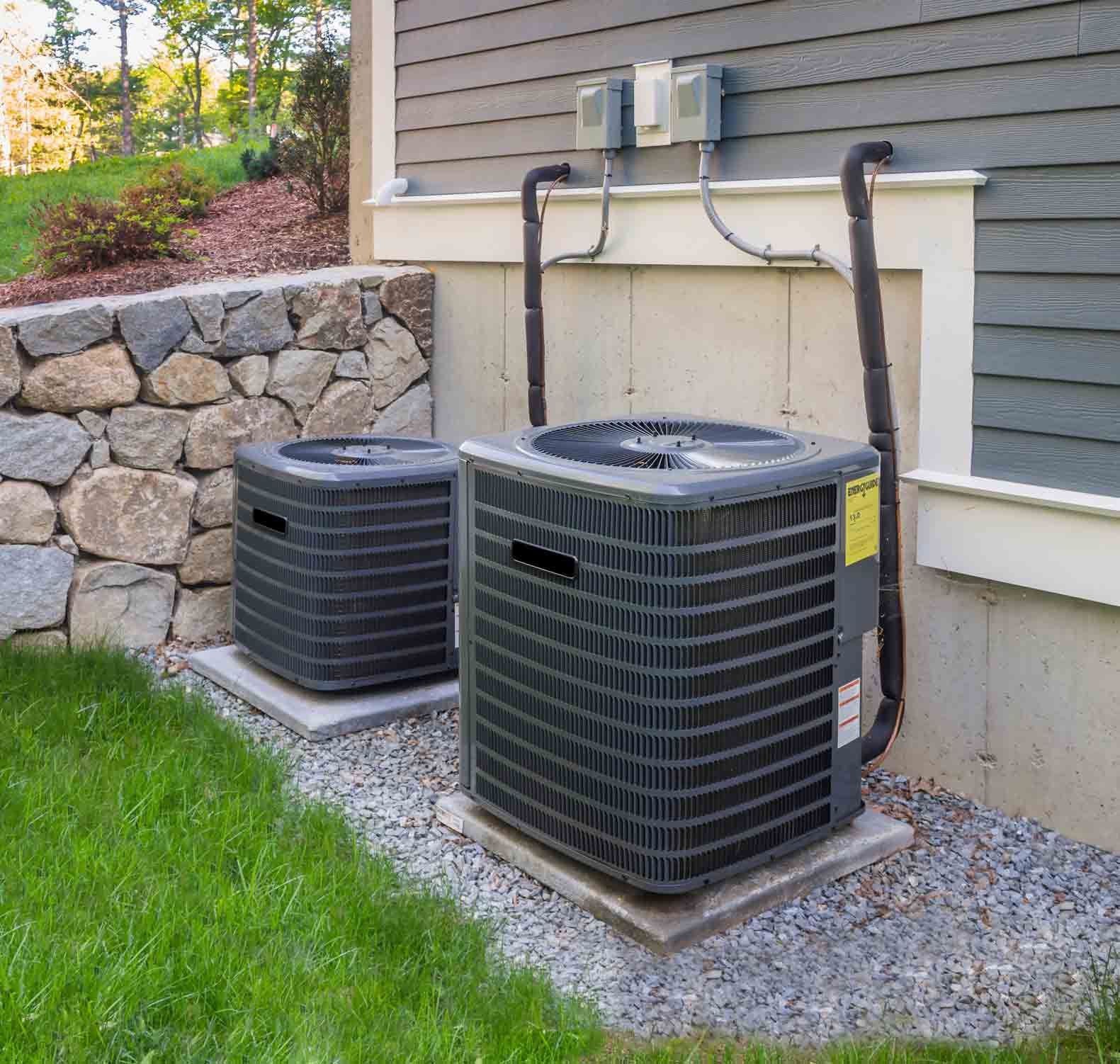 Two air conditioners are sitting outside of a house. Two air conditioners are sitting outside of a house.