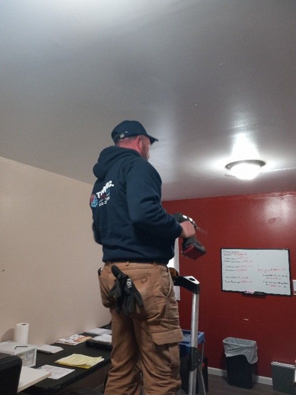 Man in cap and hoodie on a stepladder, drilling into a ceiling with a drill.