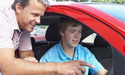 a man is teaching a young man how to drive a car .