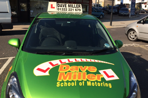 a green dave miller school of motoring car is parked in a parking lot