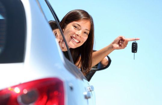 a woman is pointing at a car key while peeking out of a car window .