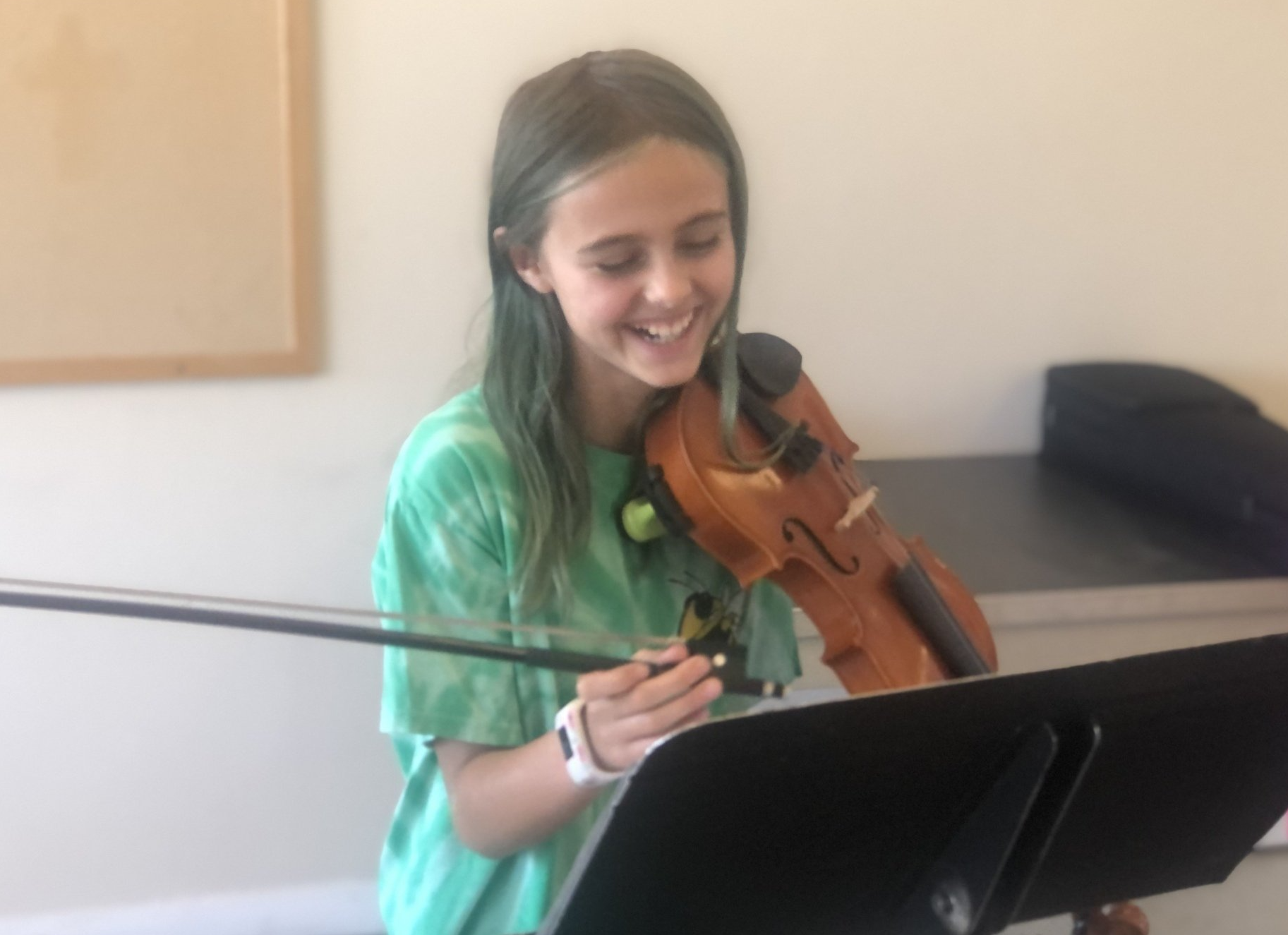 A young girl in a green shirt is playing a violin.