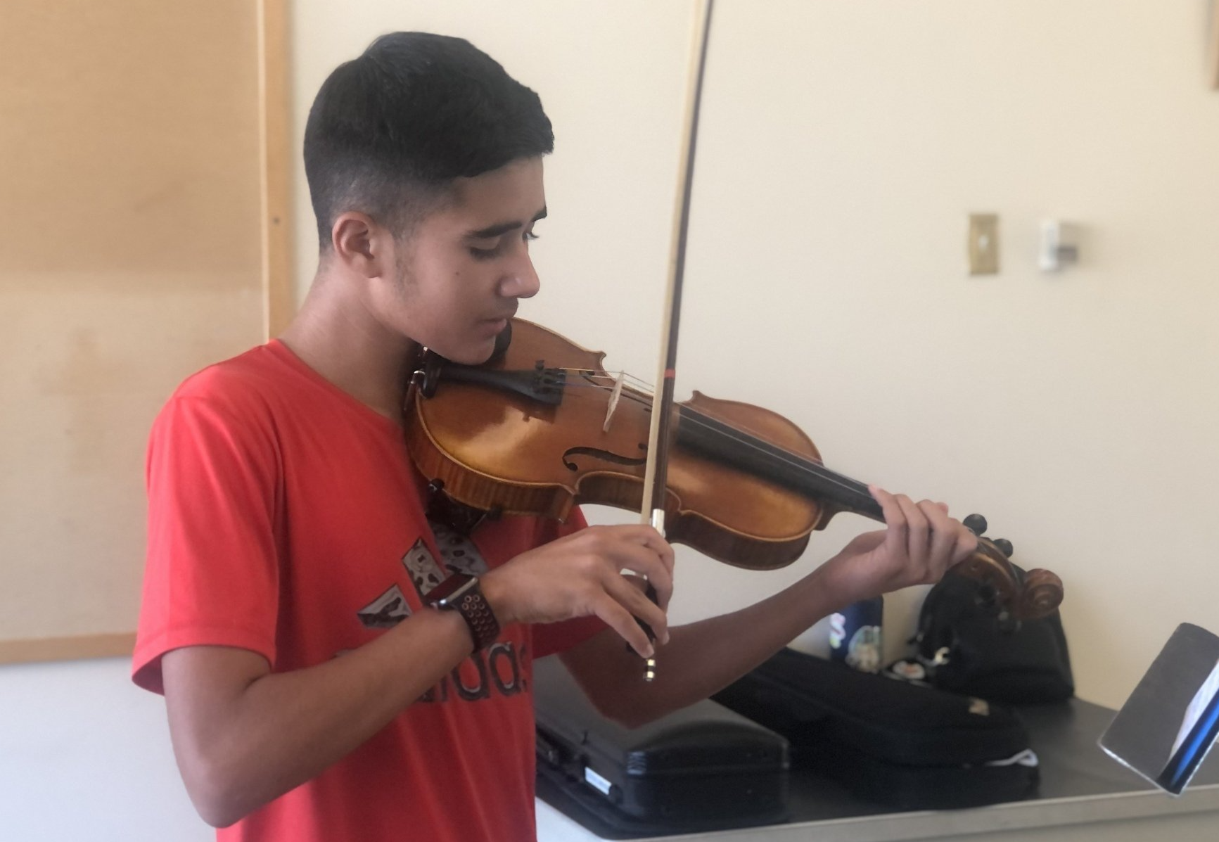 A young man in a red shirt is playing a violin